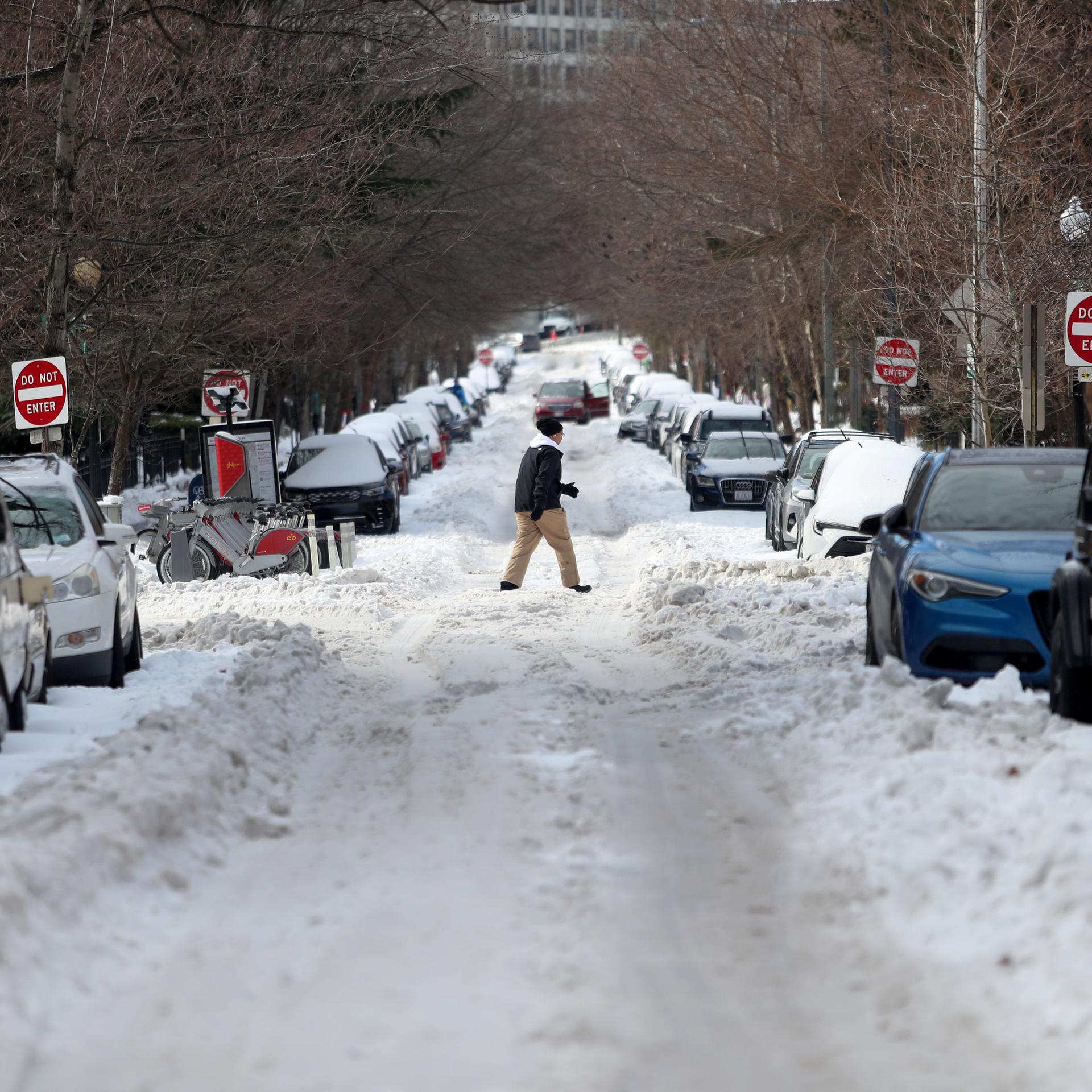 Ein Mann läuft in Washington über eine heftig verschneite Straße, viele Autos stehen am Straßenrand.