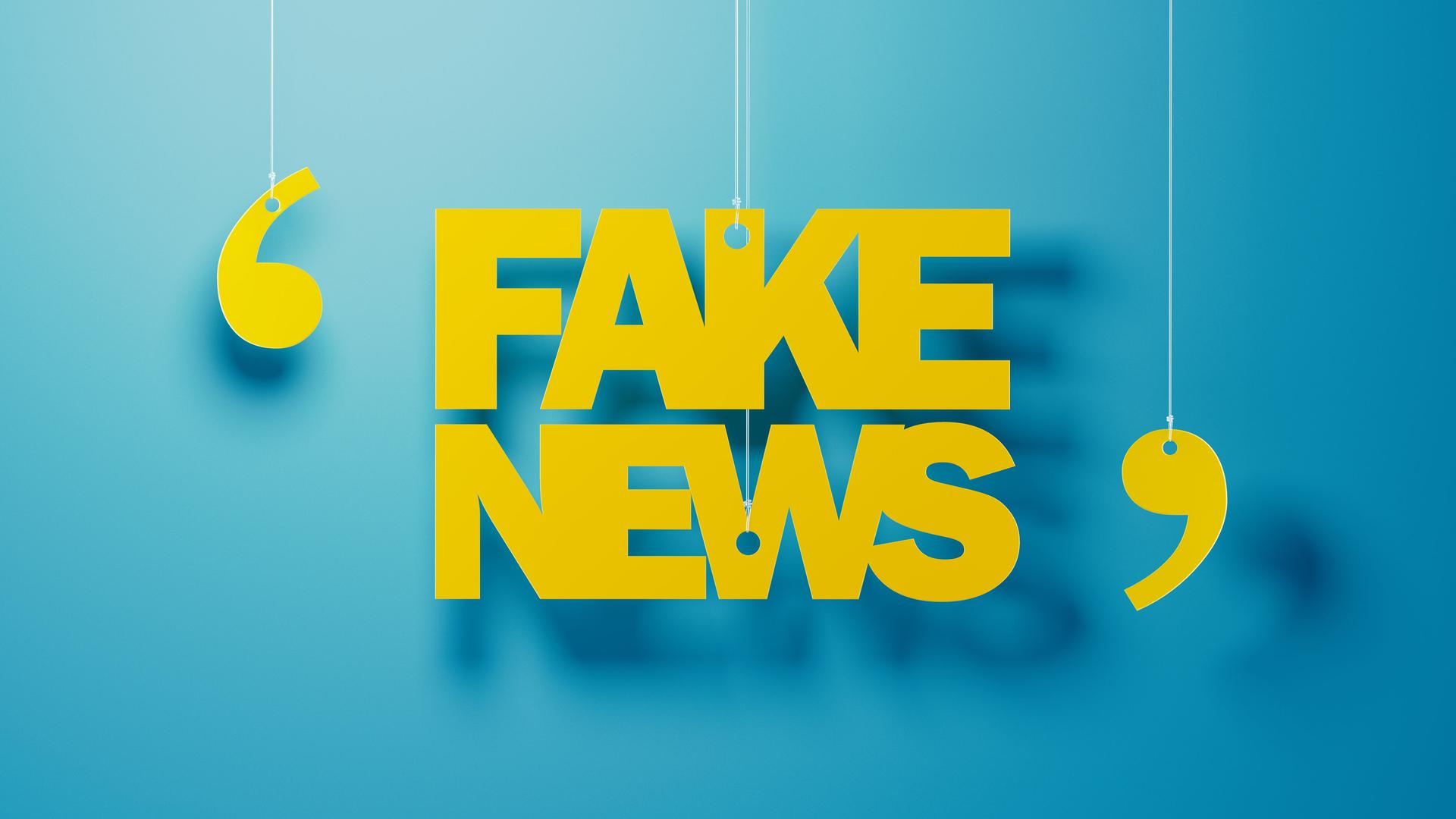 Gelbe Buchstaben hängen vor einer blauen Wand und formen das Wort "Fake News" in Anführungen