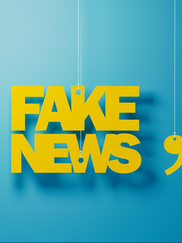 Gelbe Buchstaben hängen vor einer blauen Wand und formen das Wort "Fake News" in Anführungen