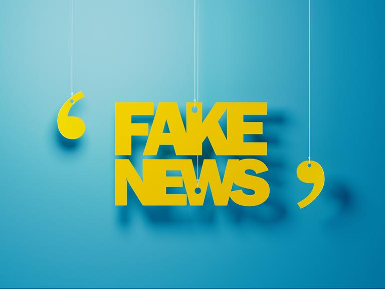 Gelbe Buchstaben hängen vor einer blauen Wand und formen das Wort "Fake News" in Anführungen