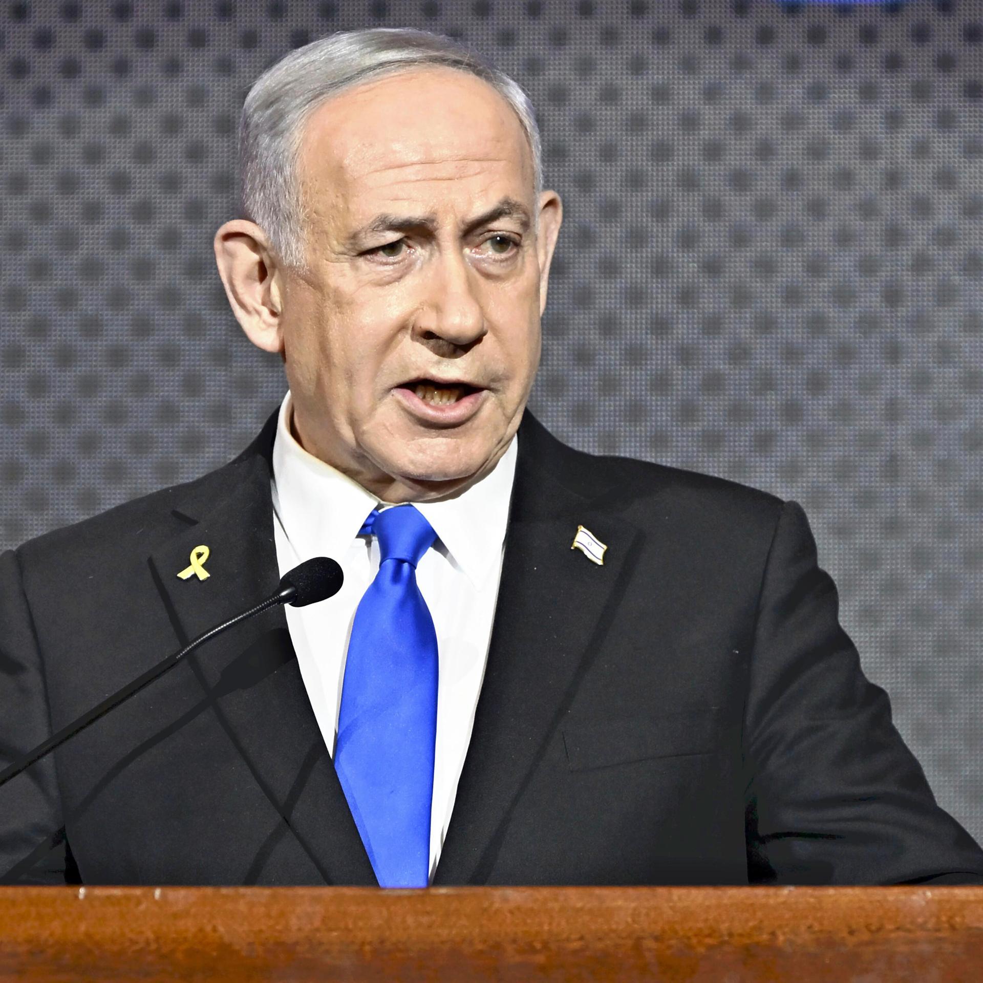 Der israelische Ministerpräsident Benjamin Netanjahu spricht im Anzug vor dunkelgrauem Hintergrund an einem Podium