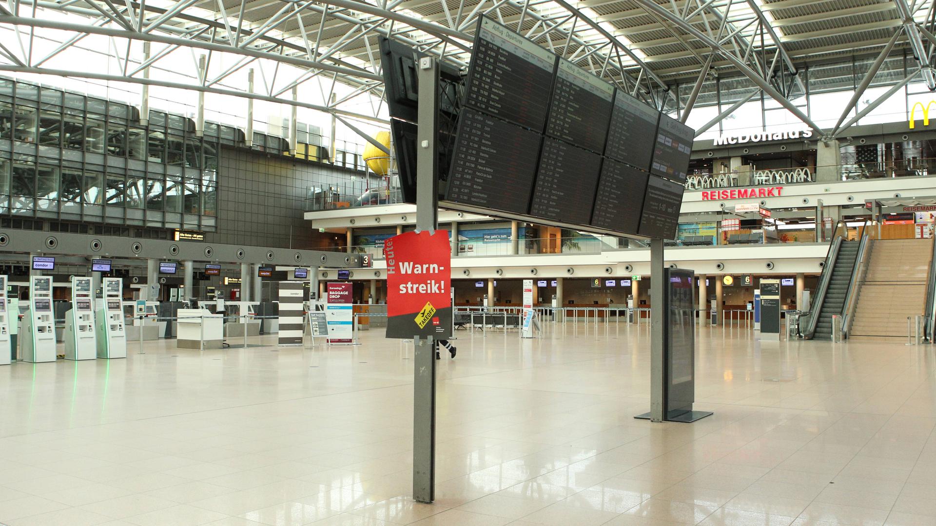 Menschenleeres Terminal 1 im Flughafen Hamburg. An der Anzeige für Ankünfte und Abflüge ist ein Plakat mit der Aufschrift "Warnstreik" angebracht.