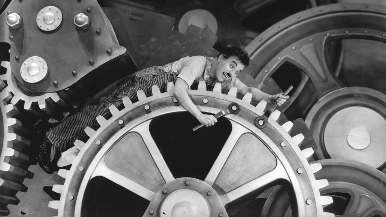 Charlie Chaplin liegt auf Zahnrädern im Stummfilm "Modern Times", 1936. 