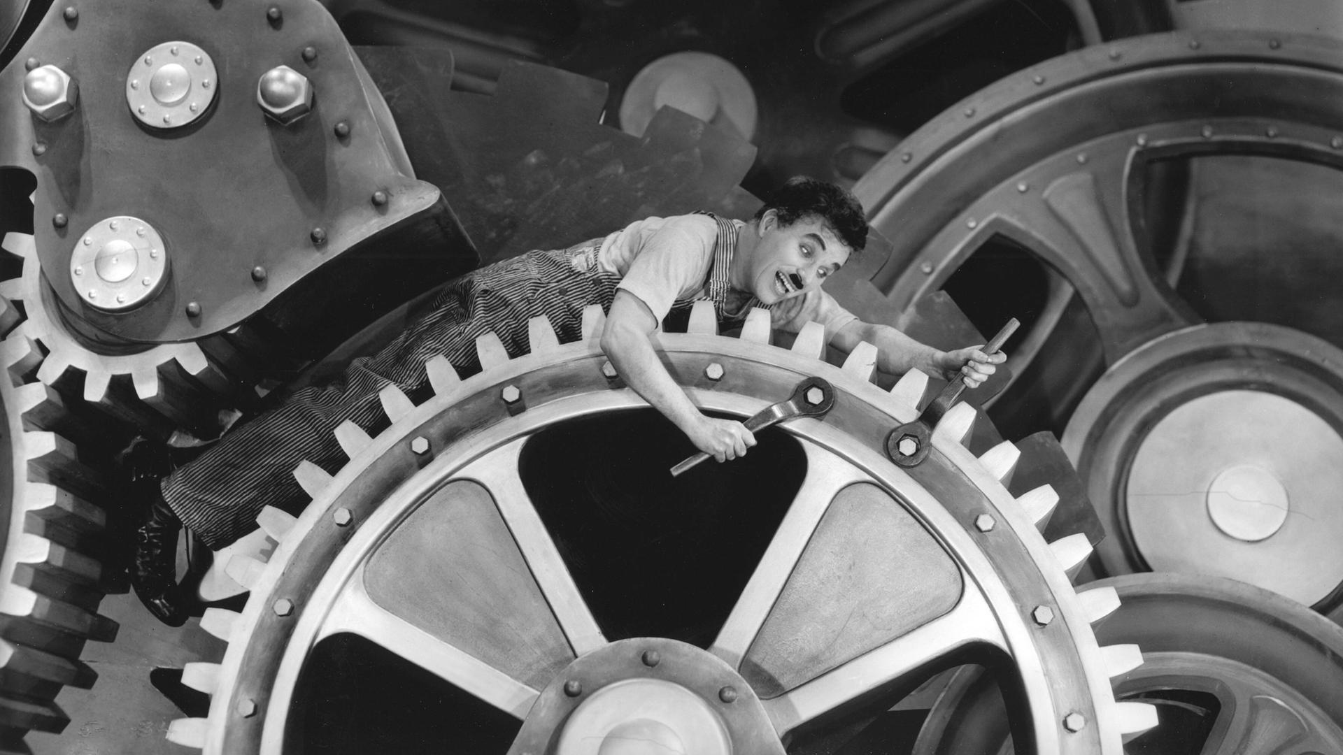 Charlie Chaplin liegt auf Zahnrädern im Stummfilm "Modern Times", 1936. 