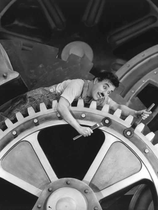 Charlie Chaplin liegt auf Zahnrädern im Stummfilm "Modern Times", 1936. 