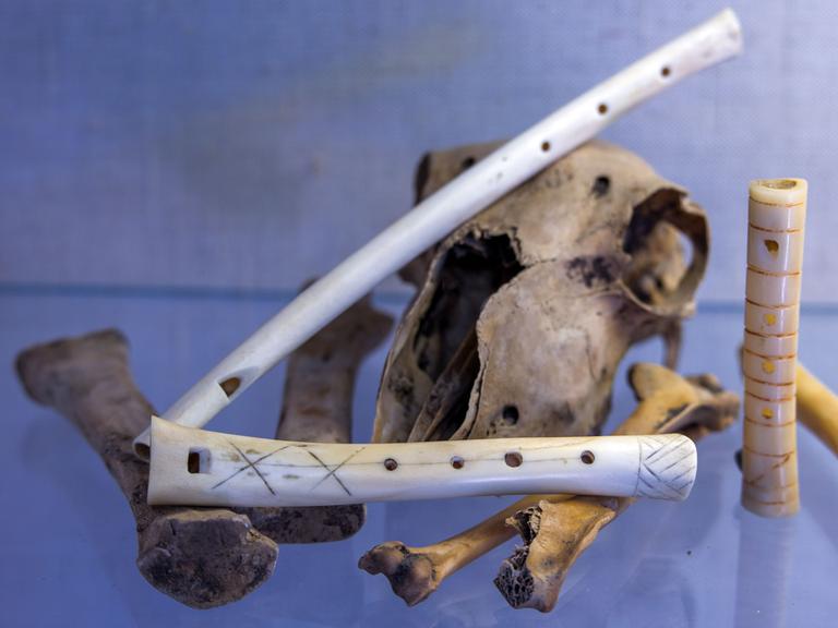 Verschieden große, nachgebaute Knochenflöten liegen auf Knochen drapiert auf einem Tisch.