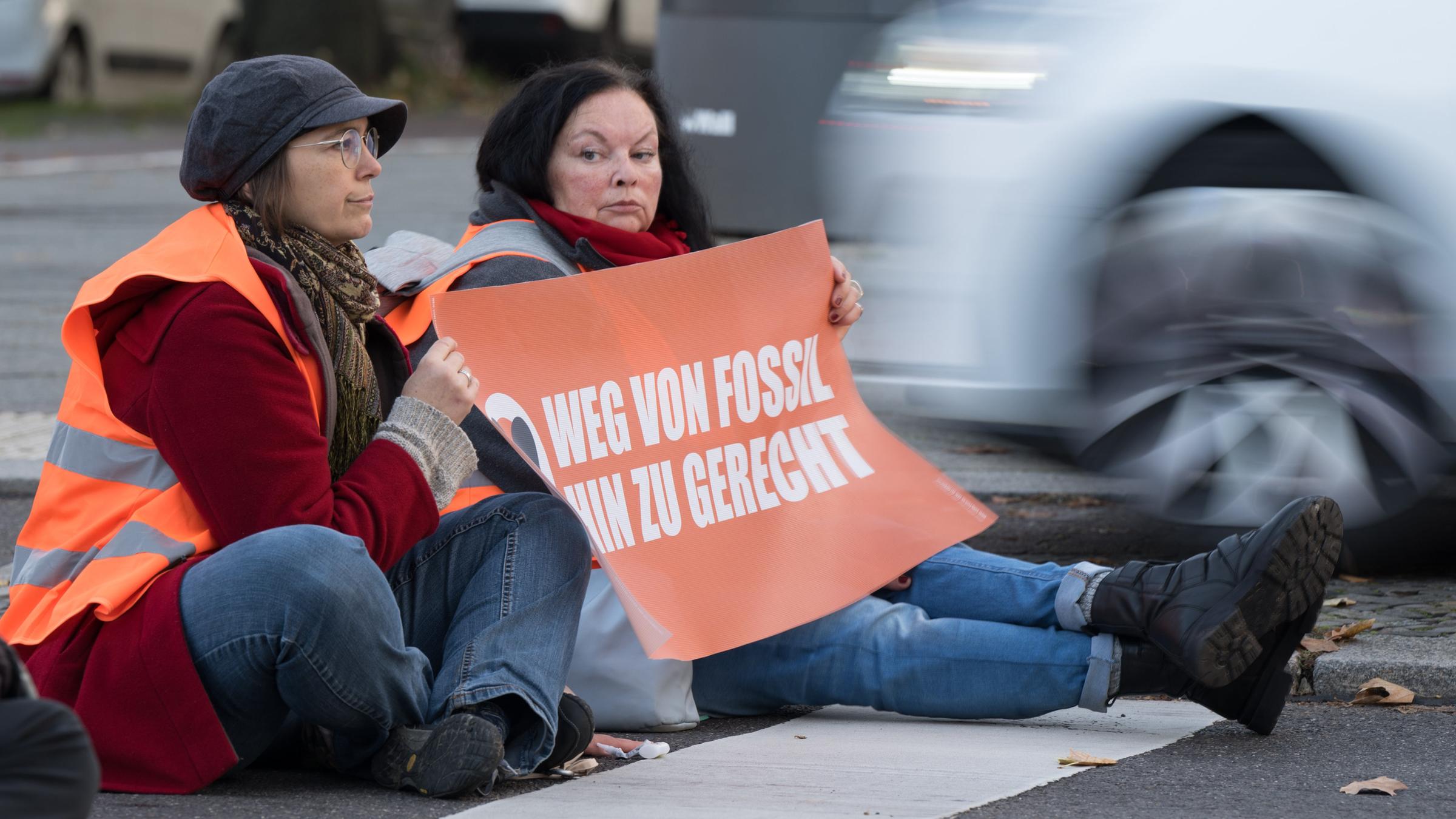 Aktivisten kleben während einer Straßenblockade der Klimaschutzgruppe "Letzte Generation" auf dem Asphalt.