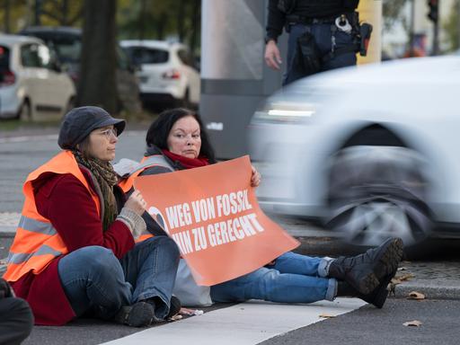 Aktivisten kleben während einer Straßenblockade der Klimaschutzgruppe "Letzte Generation" auf dem Asphalt.