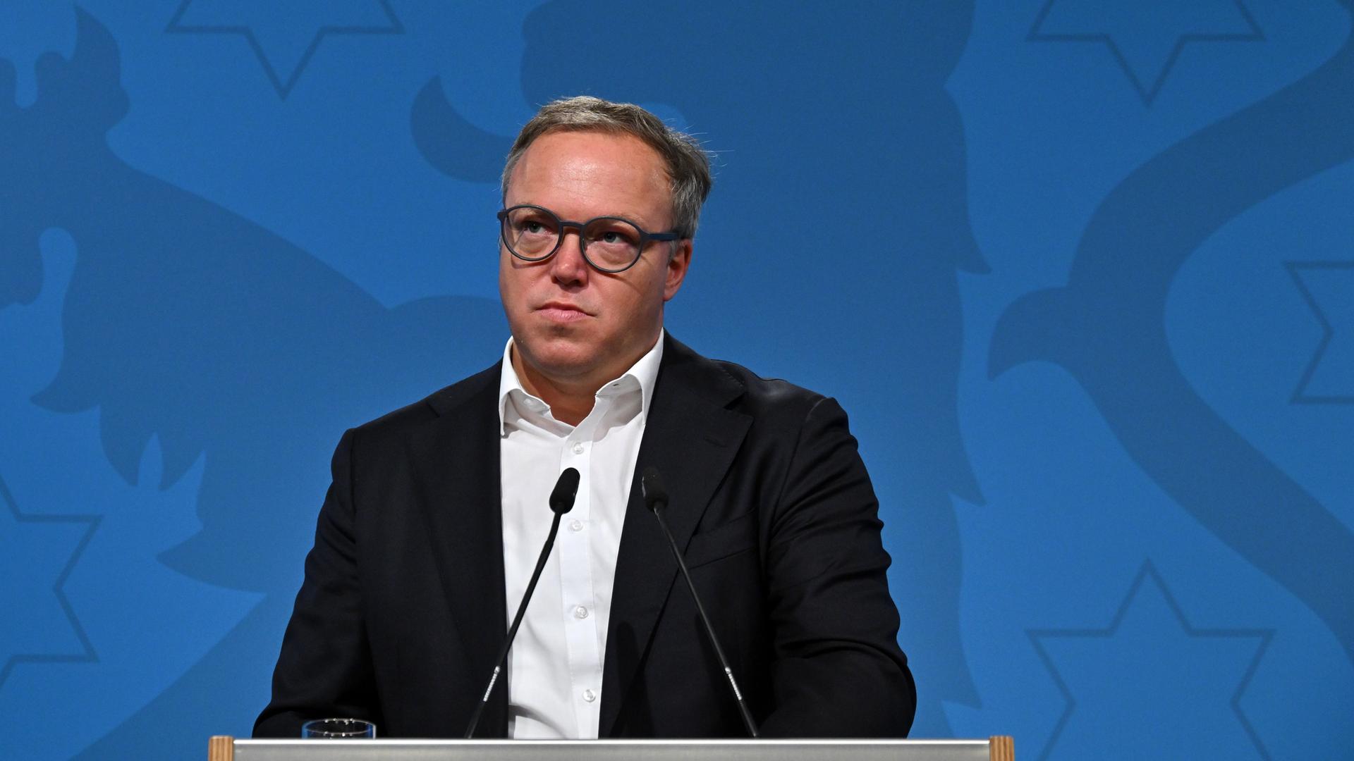 Voigt bei einer Pressekonferenz. Er steht an einem Pult mit Mikrofon. Der Hintergrund ist blau.