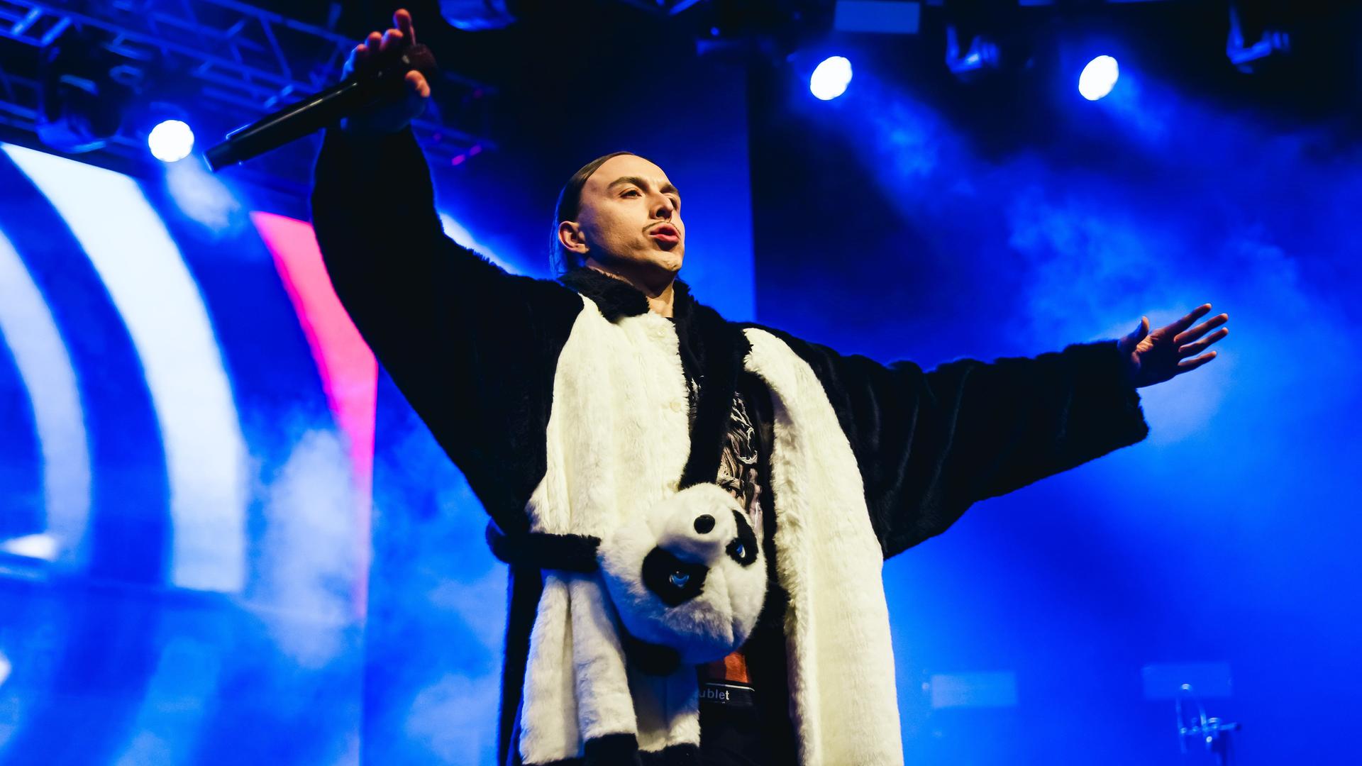 Der estnische Rapper Tommy Cash steht bei einem Konzert in der itlienischen Stadt Mailand im November 2023 mit weitausgebreiteten Armen im Pandakostum auf der Bühne. Der estnische Rapper Tommy Cash steht bei einem Konzert in der itlienischen Stadt Mailand im November 2023 mit weitausgebreiteten Armen im Pandakostum auf der Bühne.