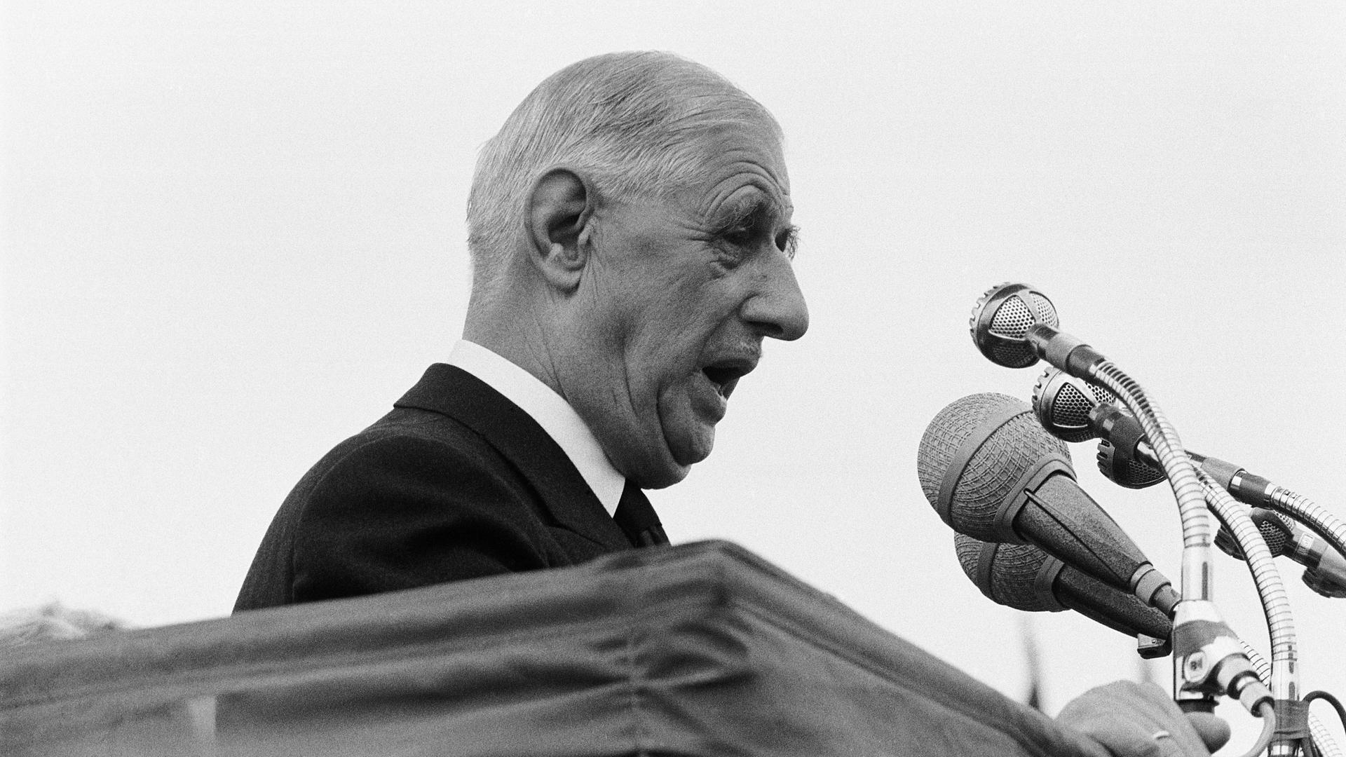 Der französische Staatspräsident Charles de Gaulle steht vor Mikrofonen an einem Pult und hält eine Rede.