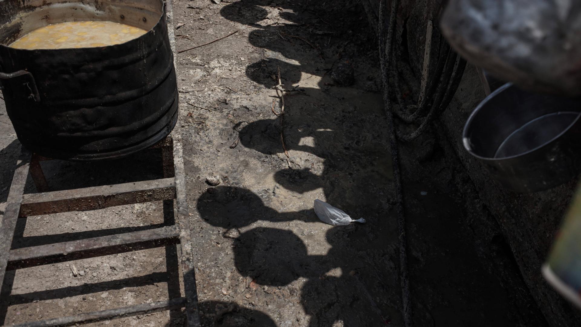 Schatten von Palästinensern mit Töpfen, die in einer Schlange warten, um warme Mahlzeiten zu erhalten.