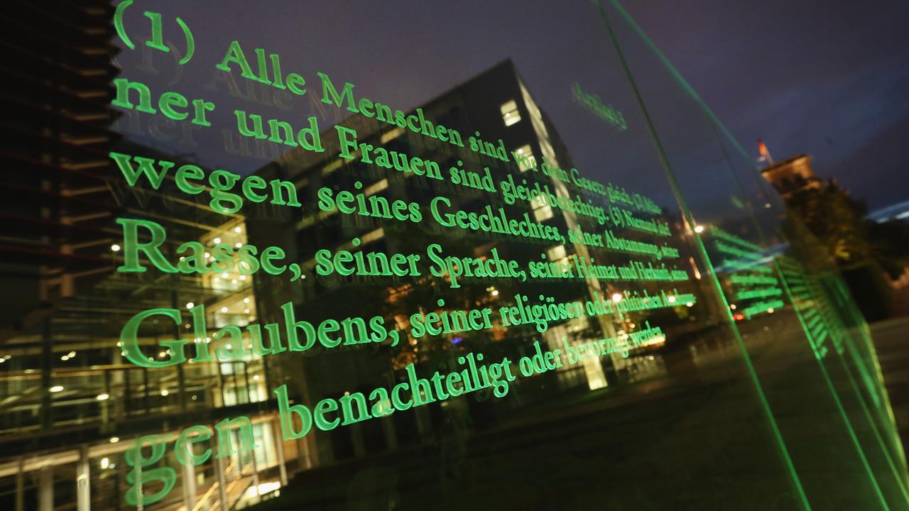 Ein Artikel des deutschen Grundgesetzes auf einer Glastafel am Reichstagsufer, Spiegelungen von Gebäuden und Lichtern.