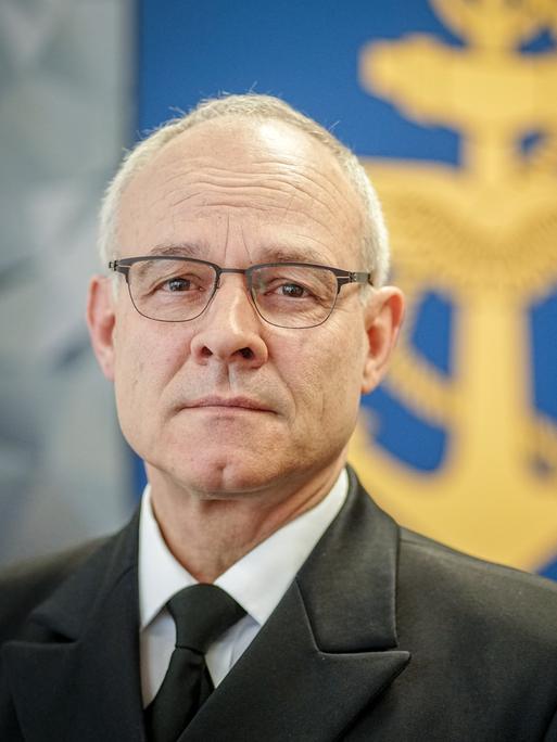 Jan Christian Kaack in seinem Büro im Verteidigungsministerium. Im Hintergrund ist ein blaues Wappen eines gelben geflügelten Ankers zu sehen, um den sich ein gelbes Seil windet.