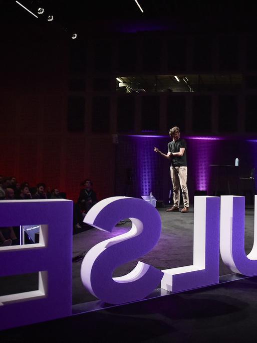 Mistral-Chef Arthur Mensch auf Europas größter Konferenz für AT "ai-PULSE". Zu sehen ist ein junger Mann auf einer Bühne und mit großen Buchstaben des Firmennamens.