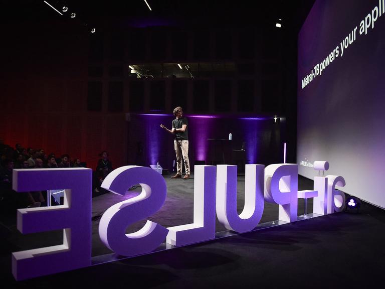 Mistral-Chef Arthur Mensch auf Europas größter Konferenz für AT "ai-PULSE". Zu sehen ist ein junger Mann auf einer Bühne und mit großen Buchstaben des Firmennamens.