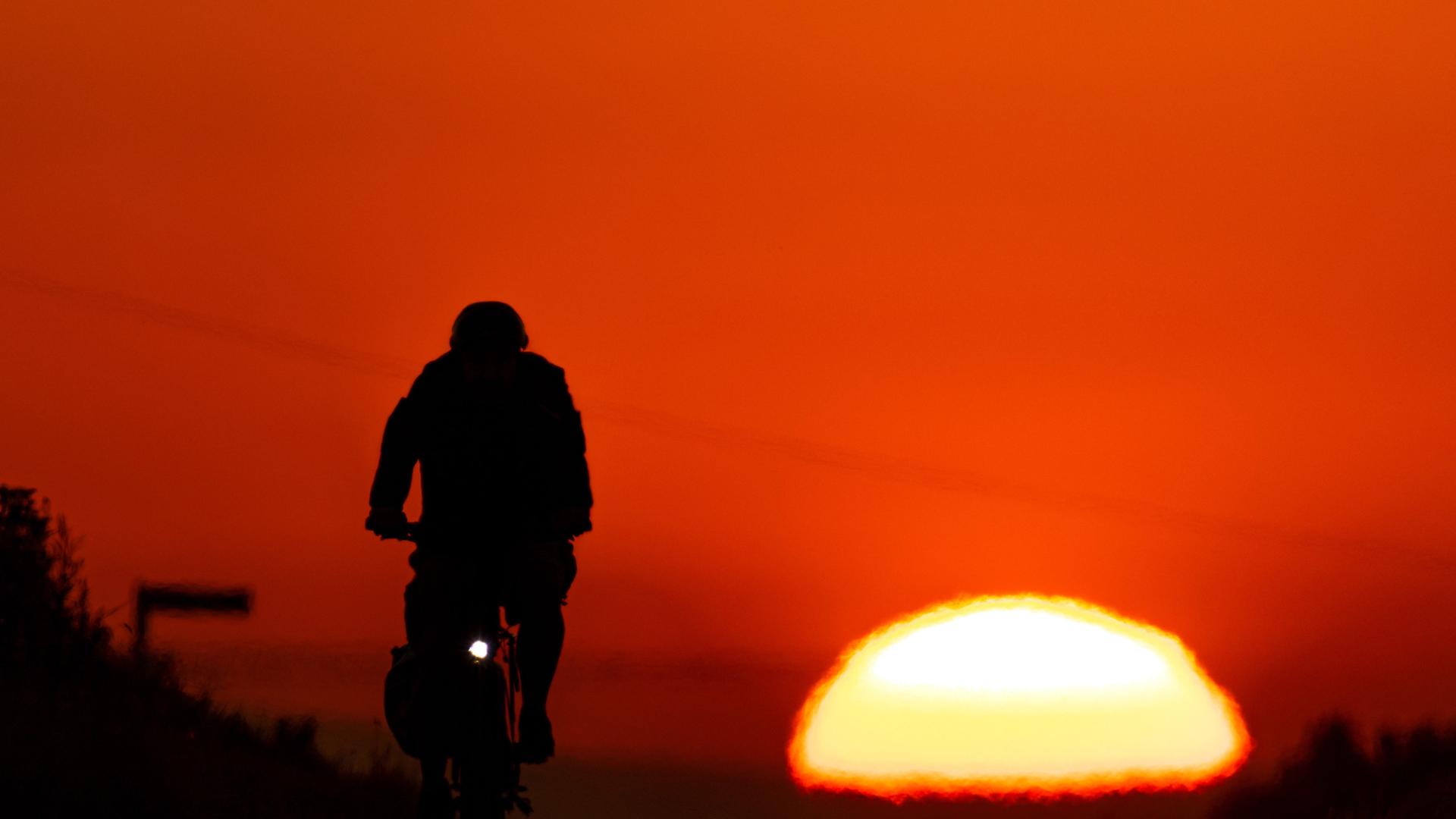Ein Fahrradfahrer radelt am frühen Morgen bei Sonnenaufgang durch die Felder bei Frankfurt am Main. 