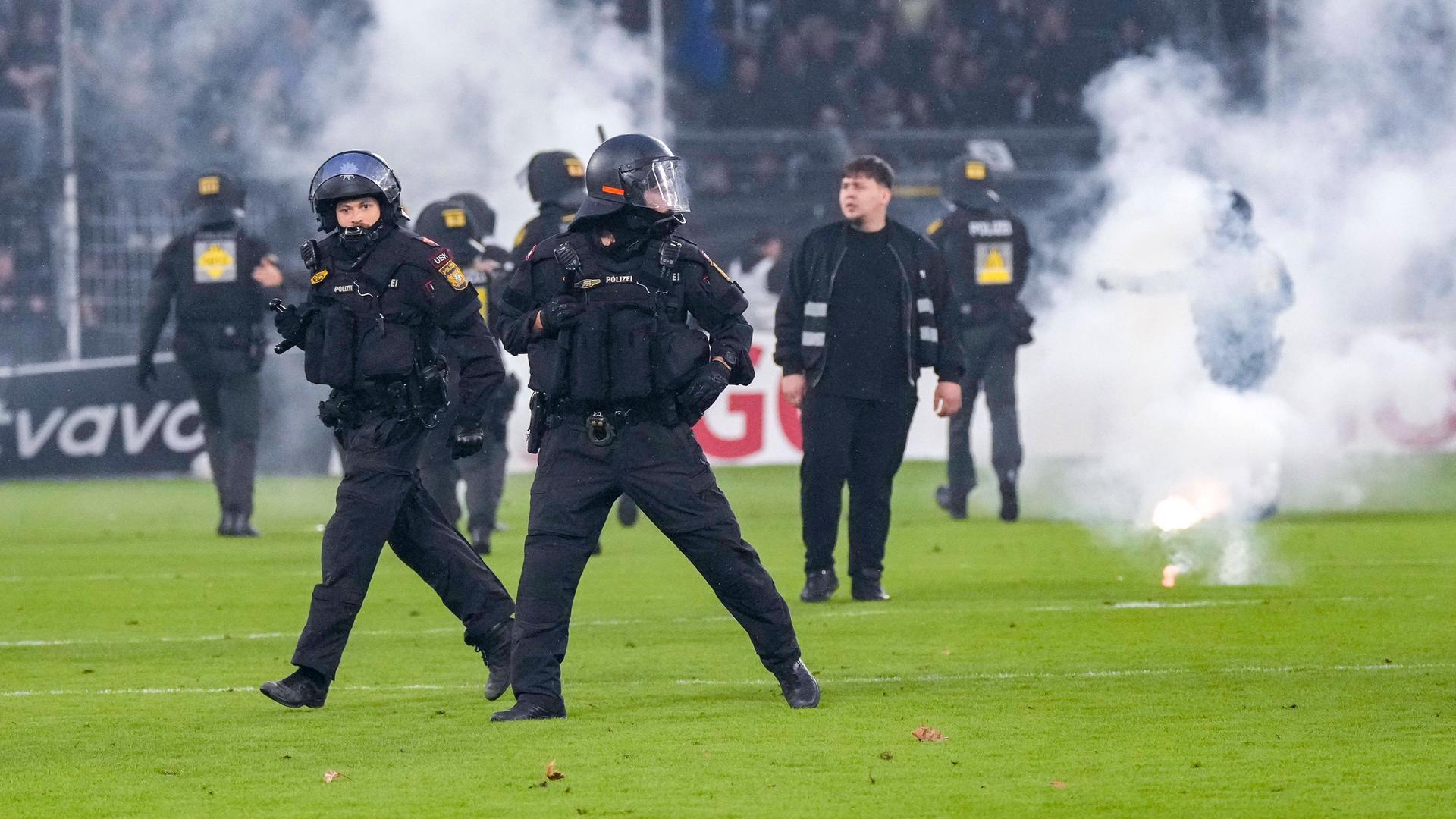 Polizisten sichern das Spielfeld nach Pyroattacken von den Rängen. Polizisten sichern das Spielfeld nach Pyroattacken von den Rängen.