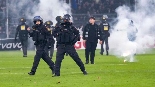 Polizisten stehen auf dem Spiel-Feld im Stadion. Es ist Rauch zu sehen.
