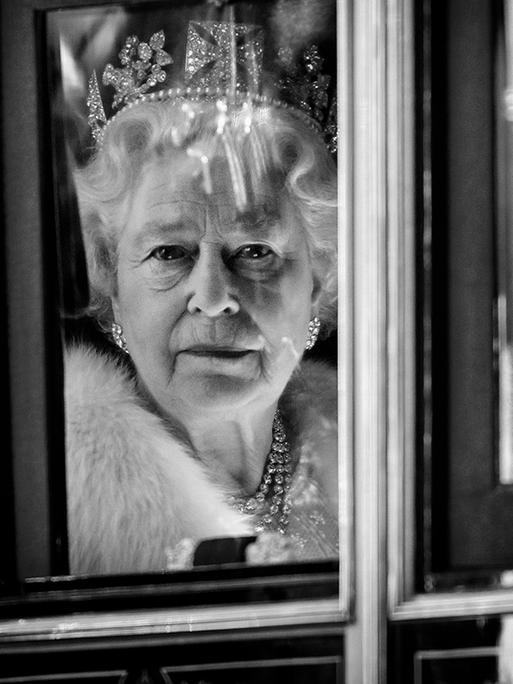 Die Queen ist durch das Fenster ihrer Kutsche zu sehen und schaut direkt in die Kamera. Sie trägt ein diamantenbesetztes Diadem.