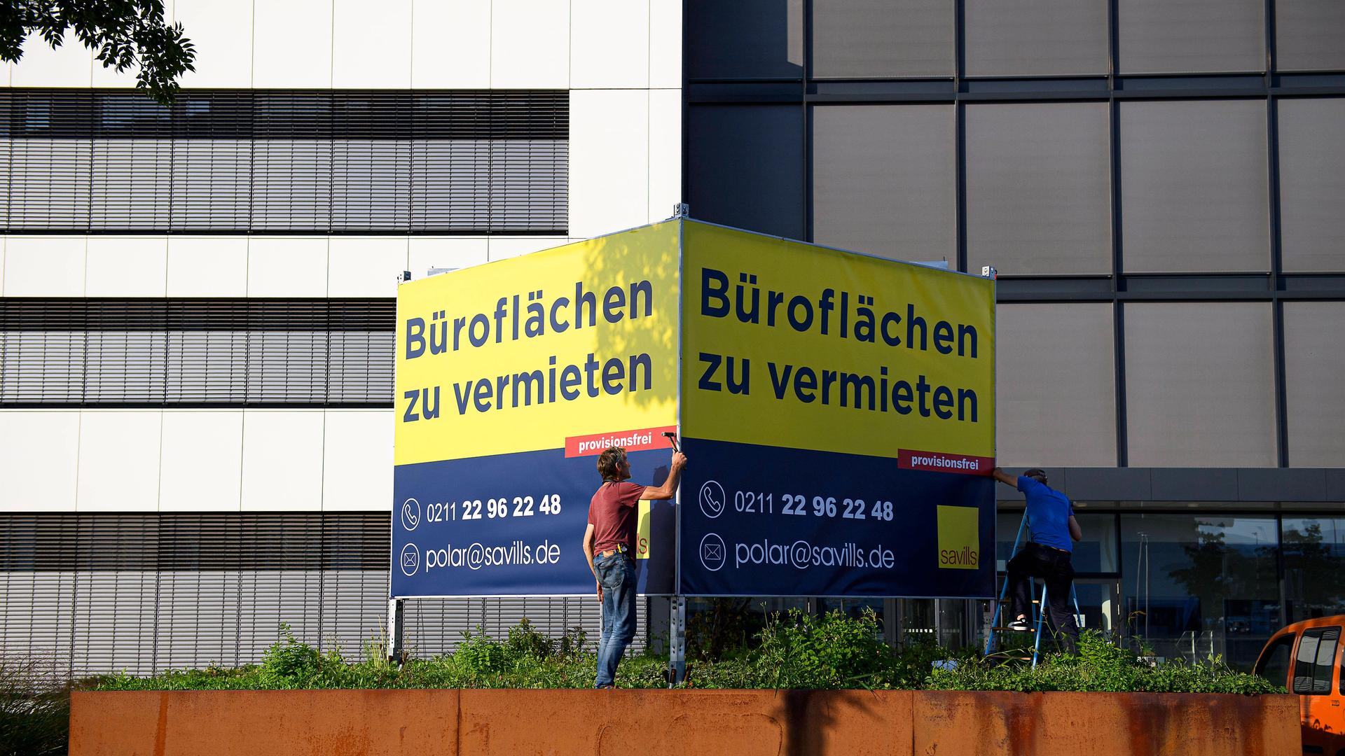 Ein Mann steht vor einem großen Schild an einem Bürogebäude, auf dem steht: "Büroflächen zu vermieten".