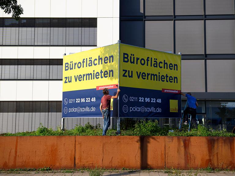 Ein Mann steht vor einem großen Schild an einem Bürogebäude, auf dem steht: "Büroflächen zu vermieten".