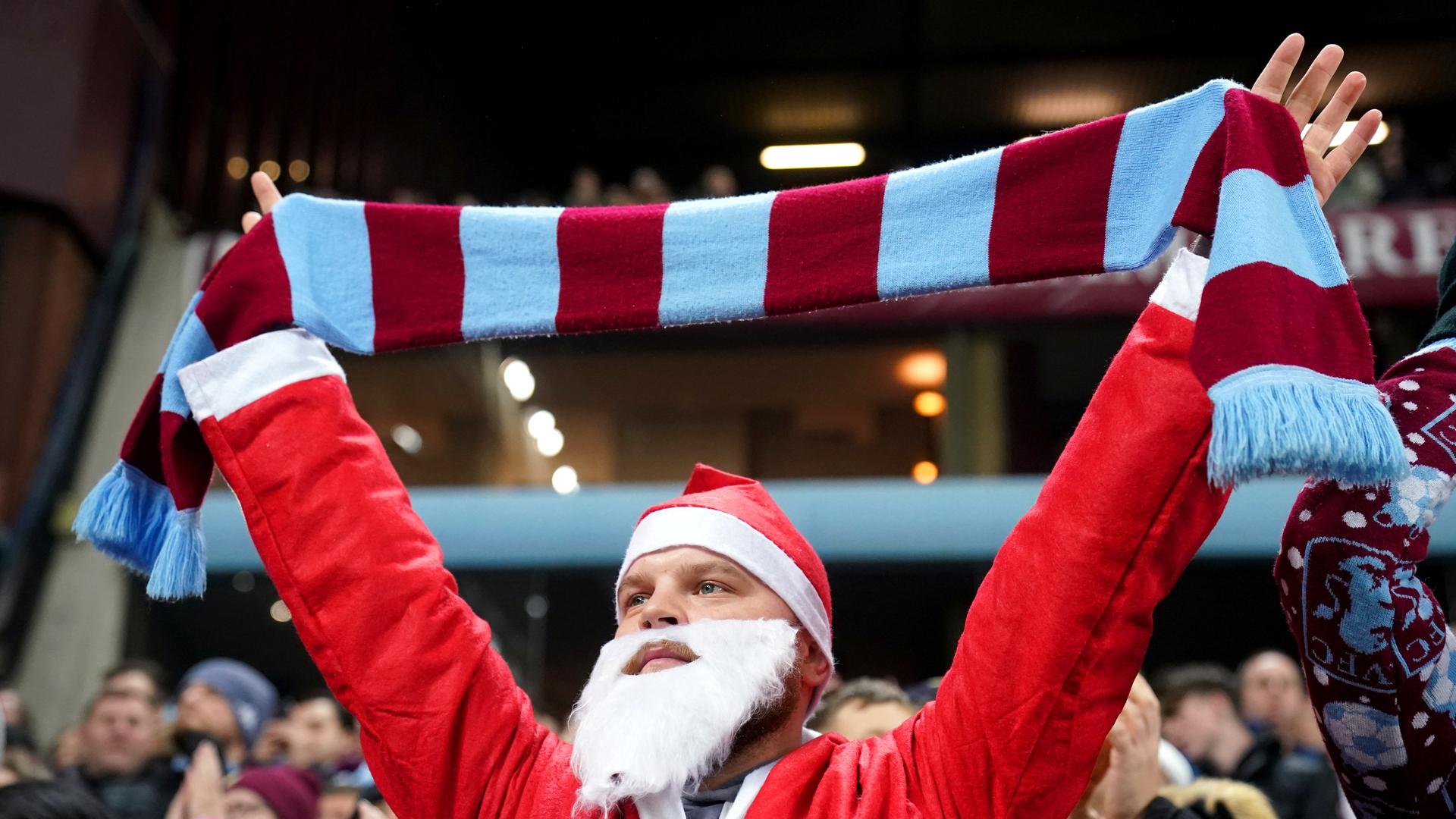 Ein Aston Villa-Fan steht als Weihnachtsmann verkleidet auf der Tribüne und hält einen Schal in die Luft. 