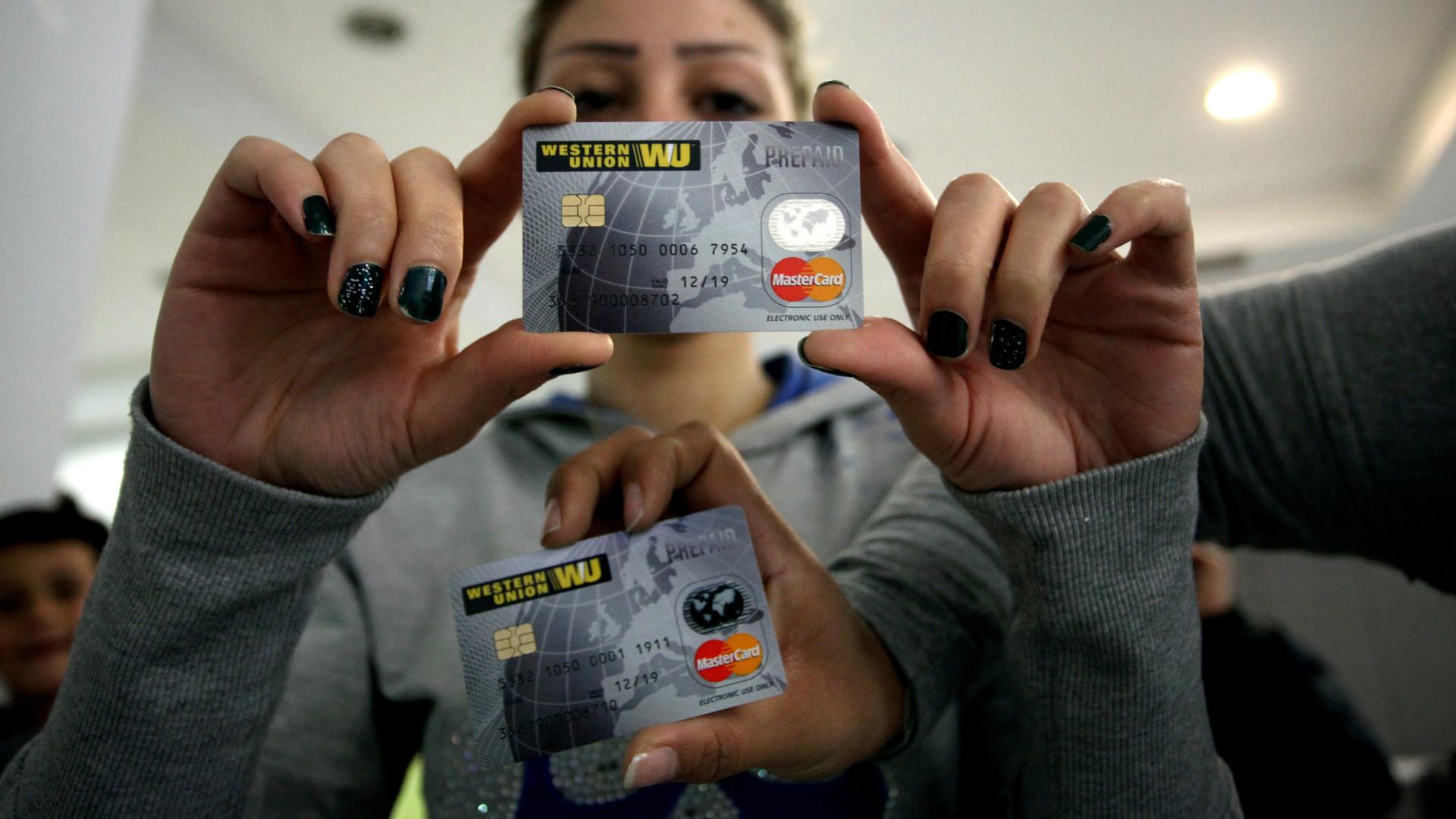 Eine Asylsuchende hält eine Pre-Paid-Kreditkarte mit Logos von Western Union und MasterCard in die Kamera.