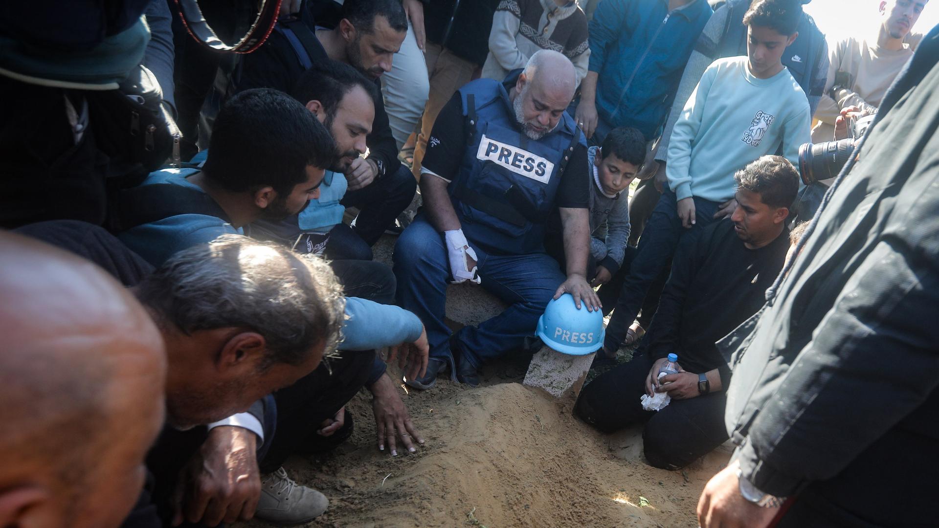 Ein blauer Helm mit der Aufschrift "Press" liegt auf dem mutmaßlichen Grab des palästinensischen Journalisten Hamza Dahdouh. Daneben knien und sitzen Jungen und Männer, einer davon trägt eine Presseweste.