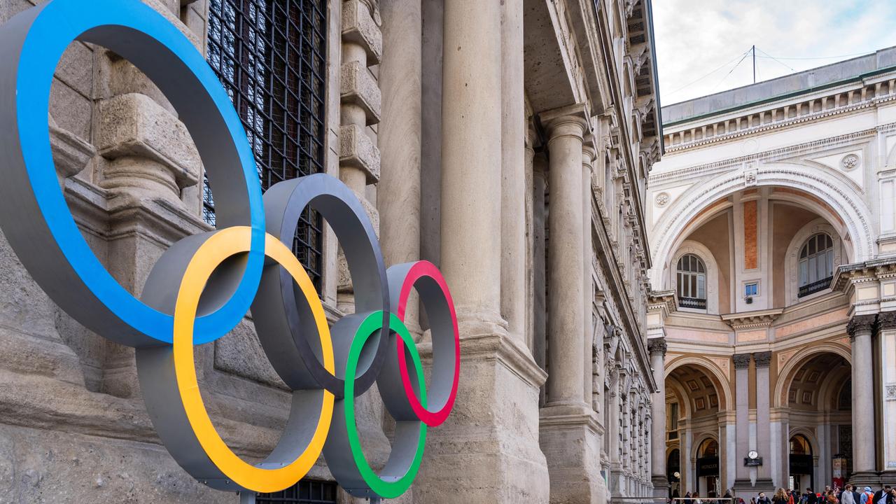 Olympische Ringe an der Fassade des Mailänder Rathauses, die von der Seite fotografiert ist. Im Hintergrund ein weiteres historisches Gebäude.