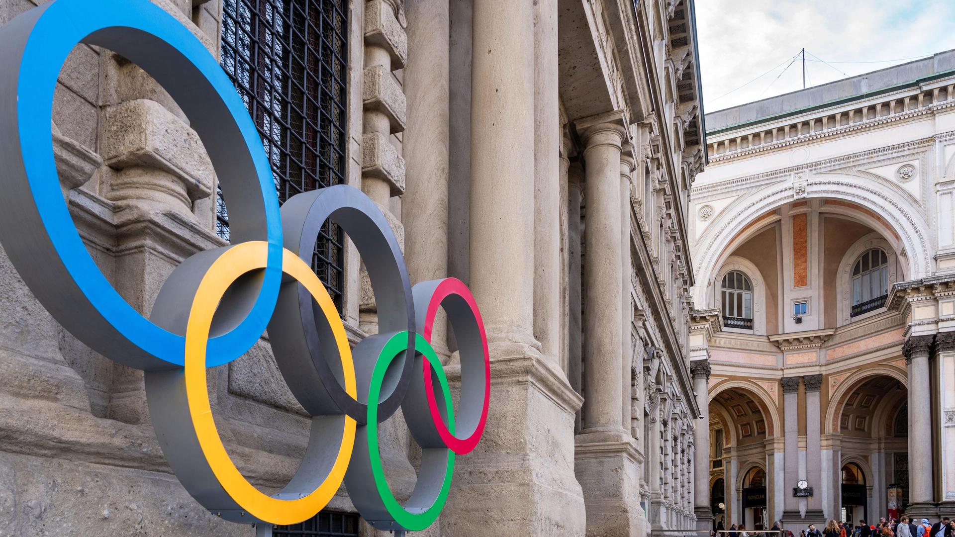 Olympische Ringe an der Fassade des Mailänder Rathauses, die von der Seite fotografiert ist. Im Hintergrund ein weiteres historisches Gebäude. Olympische Ringe an der Fassade des Mailänder Rathauses, die von der Seite fotografiert ist. Im Hintergrund ein weiteres historisches Gebäude.