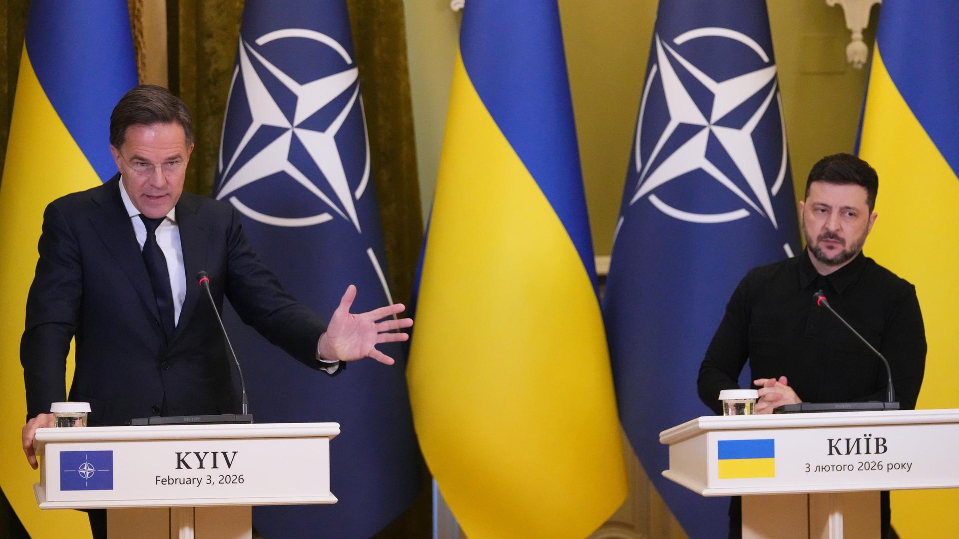 NATO-Generalsekretär Rutte und der ukrainische Präsident Selenskyj stehen nebeneinander an Rednerpulten. Hinter ihnen die Landes- und die NATO-Fahnen