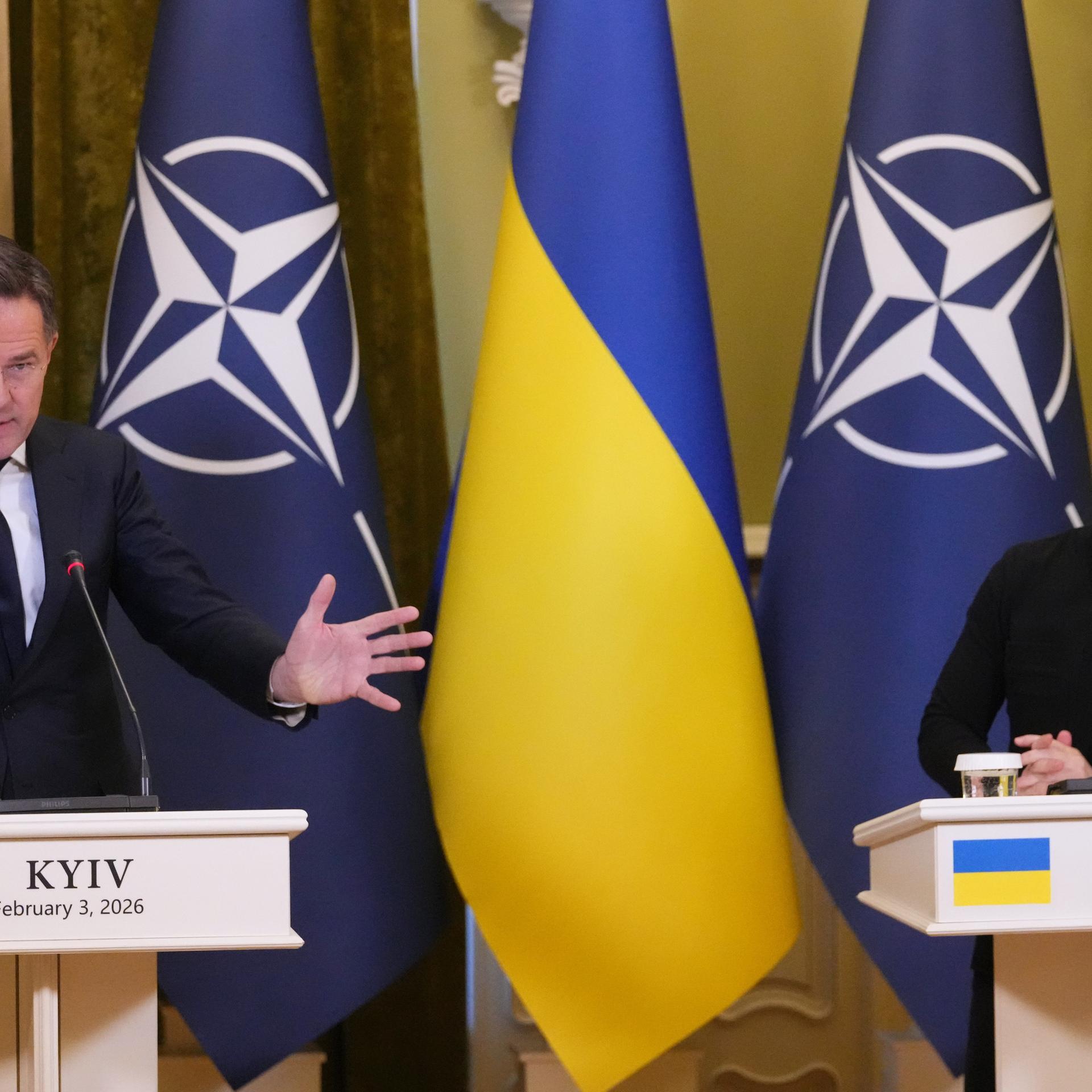 NATO-Generalsekretär Rutte und der ukrainische Präsident Selenskyj stehen nebeneinander an Rednerpulten. Hinter ihnen die Landes- und die NATO-Fahnen