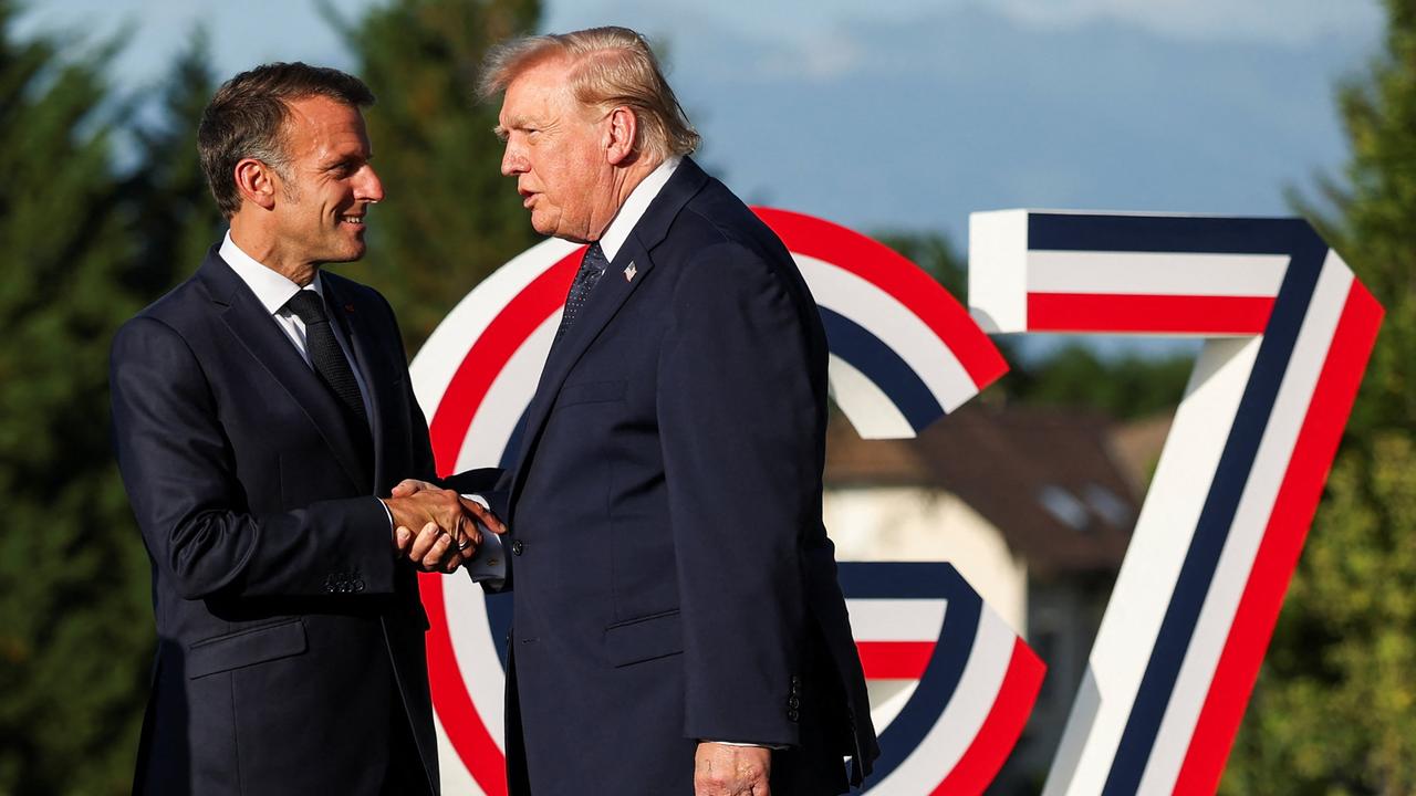 Der französische Präsident Emmanuel Macron (l.) begrüßt US-Präsident Donald Trump während des G7-Gipfels. Im Hintergrund ist das Logo des G7-Gipfels, eine überdimensional große Kombination aus G und 7 aufgestellt. Das Logo ist blau-weiß-rot gestreift.
