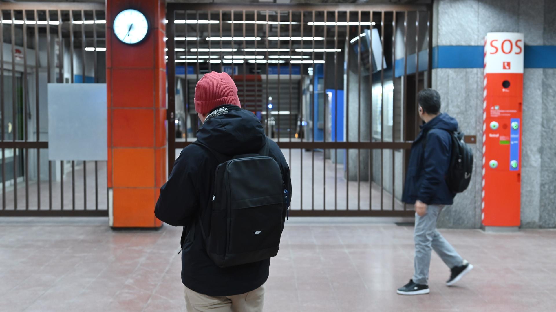 Zwei Menschen mit Rucksäcken stehen vor einer U-Bahn-Station. Die Station ist mit Gittern verschlossen. 