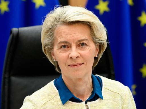 EU-Kommissionspräsidentin von der Leyen schaut in die Kamera. Hinter ihr Fahnen der EU.