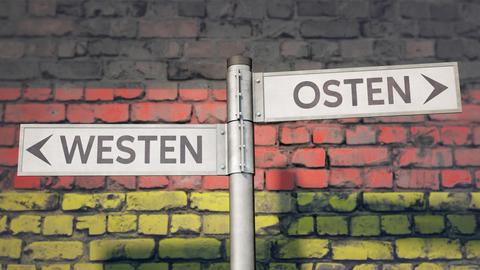 Symbolbild zum Thema Unterschiede zwischen Westdeutschland und Ostdeutschland: Ein Wegweiser weist nach Westen, der andere nach Osten.