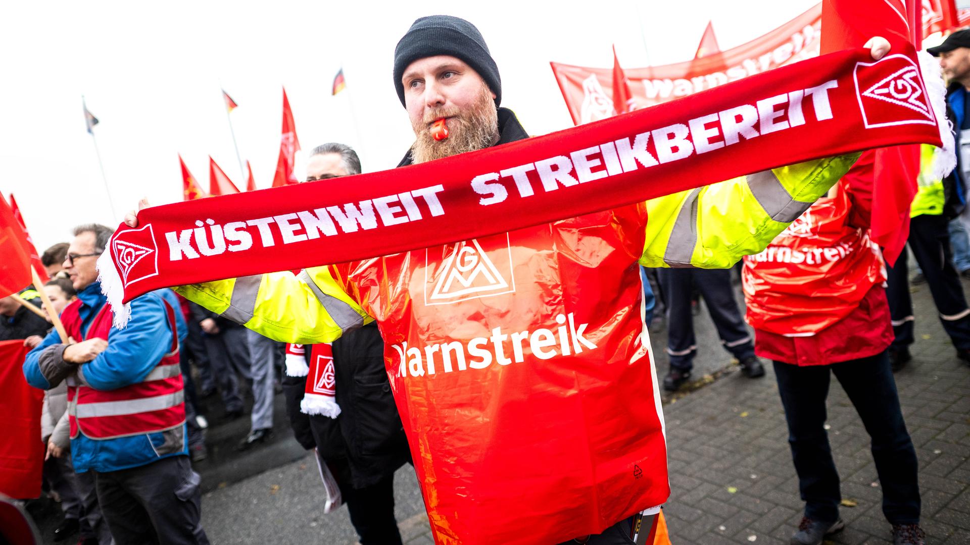 Ein Mann hält bei der Streikkundgebung von der IG Metall vor dem Volkswagen-Werk  in Emden einen Schal mit der Aufschrift "Küstenweit Streikbereit" am 2.Dezember 2024.