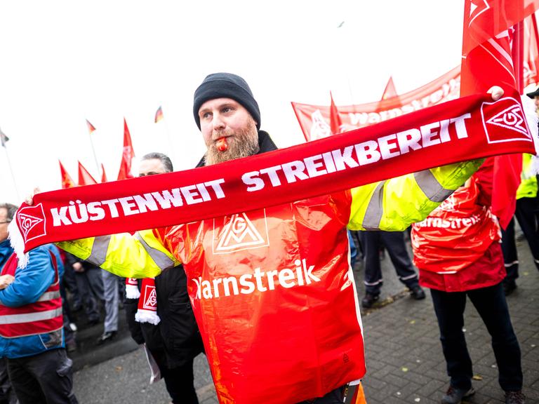 Ein Mann hält bei der Streikkundgebung von der IG Metall vor dem Volkswagen-Werk  in Emden einen Schal mit der Aufschrift "Küstenweit Streikbereit" am 2.Dezember 2024.