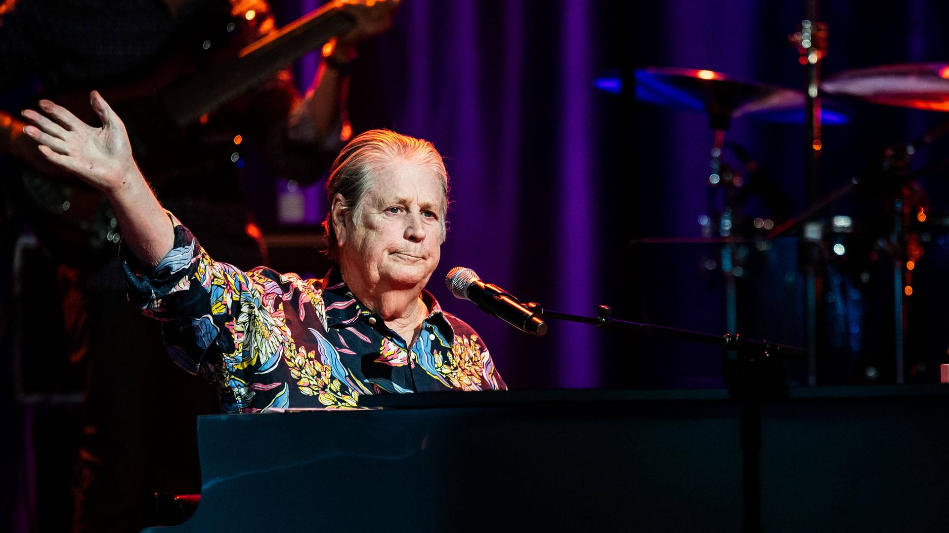 Brian Wilson sitzt in einem bunten Hemd am Konzertflügel, im Hintergrund die Band. Brian Wilson sitzt in einem bunten Hemd am Konzertflügel, im Hintergrund die Band.