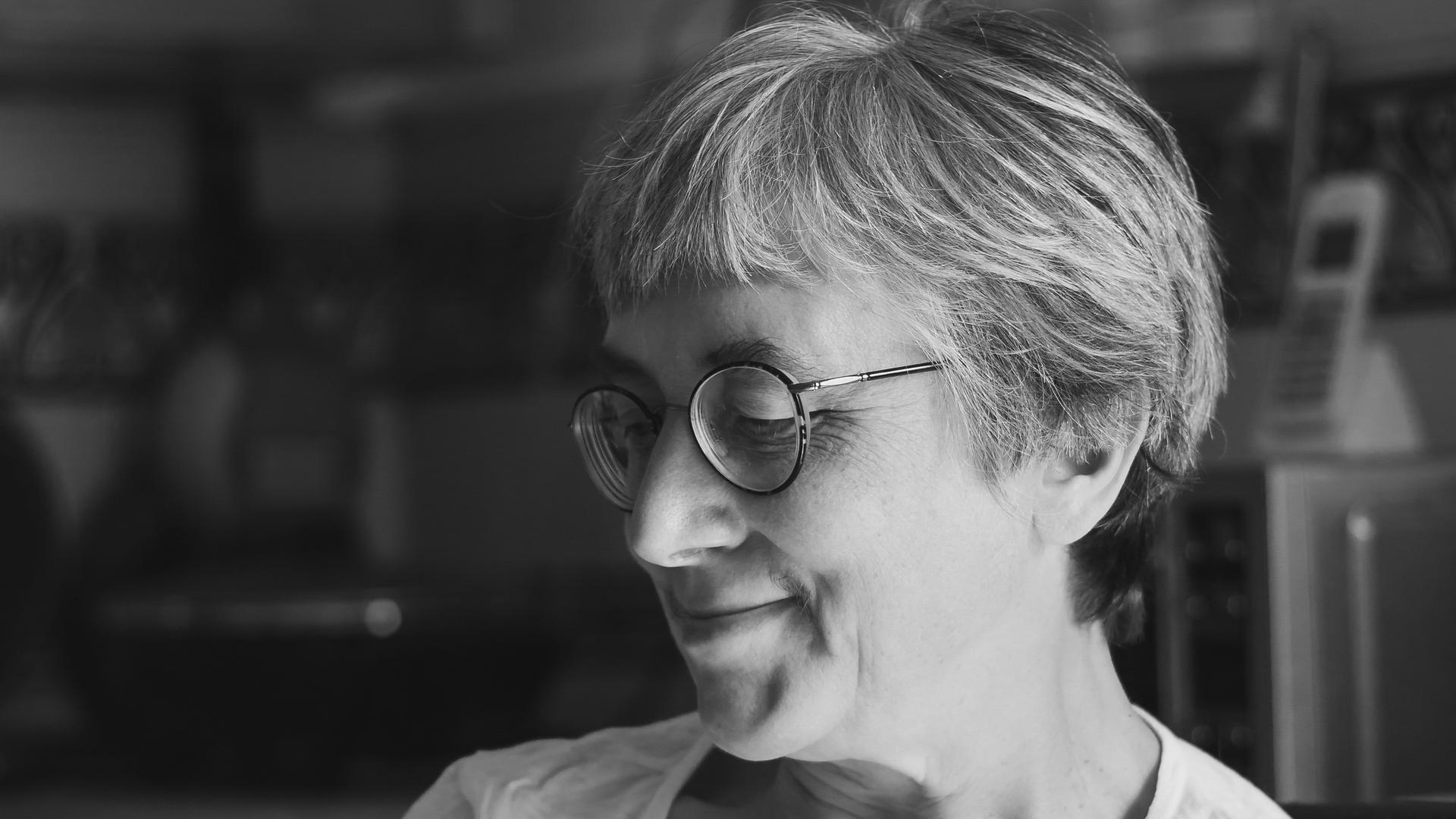 Eine Frau mit kurzen Haaren und Brille sitzt versonnen lächelnd am Tisch Eine Frau mit kurzen Haaren und Brille sitzt versonnen lächelnd am Tisch