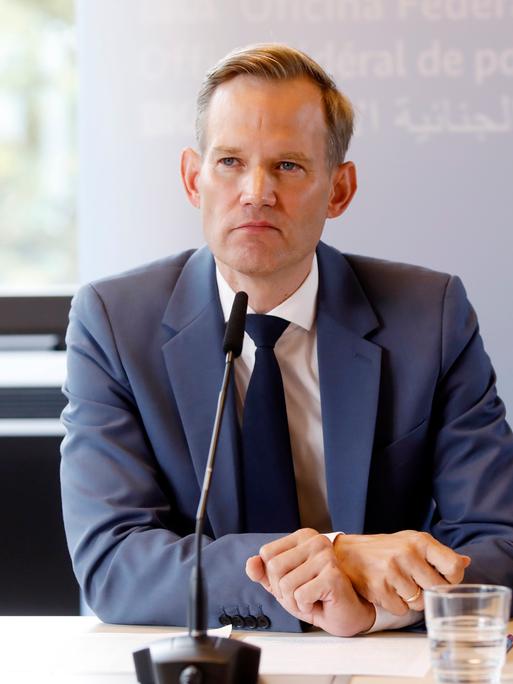 Ein Mann blick bei einer Pressekonferenz in die Kamera. Vor ihm ist ein Mikrofon. Er trägt einen dunklen Anzug, mit weißem Hemd und Kravatte. Es ist Hendrik Streeck, der Drogen- und Suchtbeauftragte der Bundesregierung.