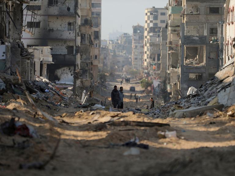 Palästinenser gehen an den Überresten zerstörter Gebäude in Gaza-Stadt vorbei.