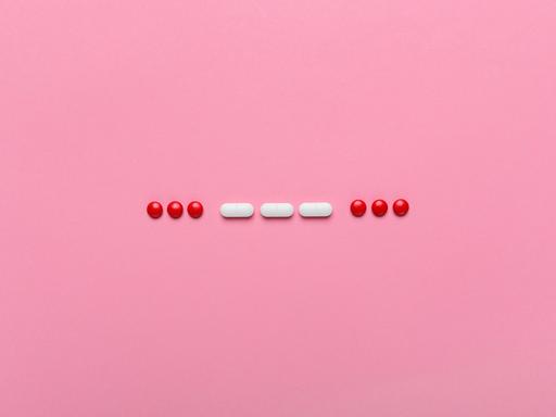 SOS Morsecode aus Pillen gelegt auf einem rosa Hintergrund.