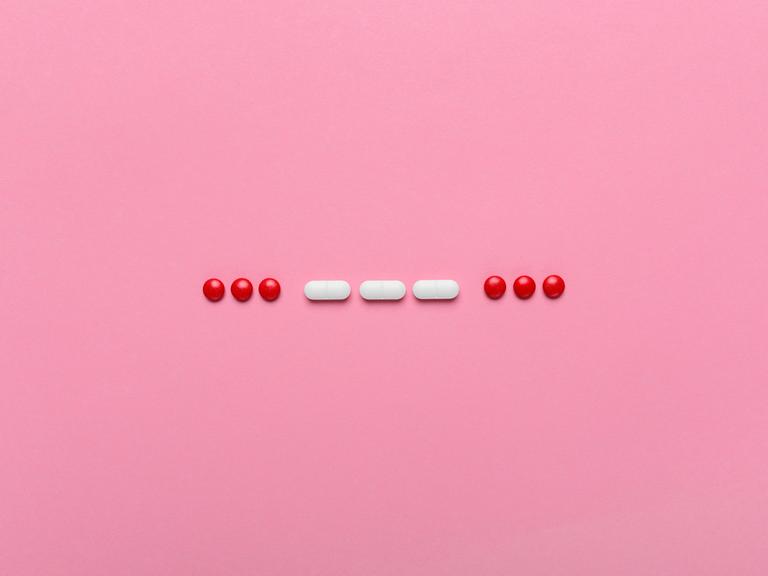 SOS Morsecode aus Pillen gelegt auf einem rosa Hintergrund.