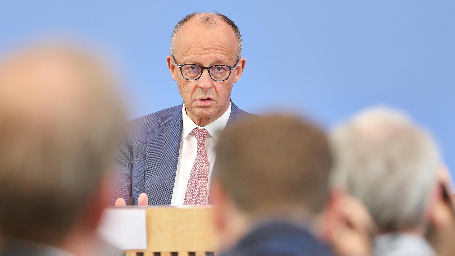 Friedrich Merz sitzt vor dem blauen Hintergrund der Bundespressekonferenz und spricht mit Journalisten.