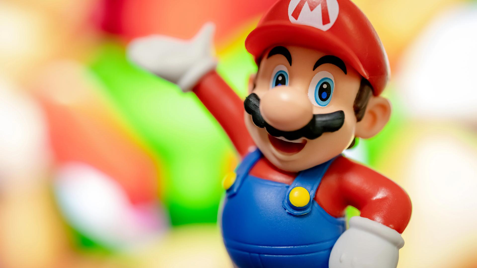 Eine Spielzeugfigur: Super Mario mit roter Mütze, Latzhose und Schnurrbart winkt und lacht.