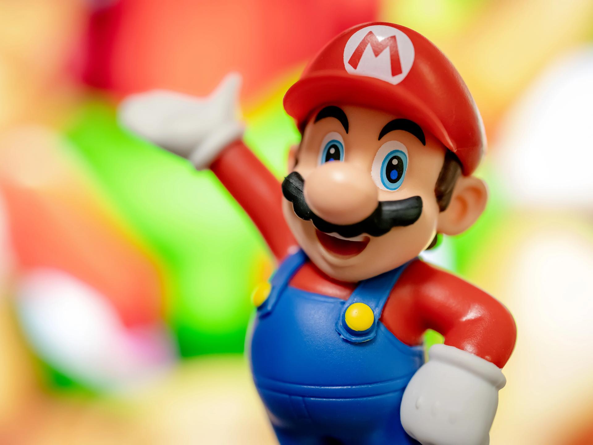 Eine Spielzeugfigur: Super Mario mit roter Mütze, Latzhose und Schnurrbart winkt und lacht.