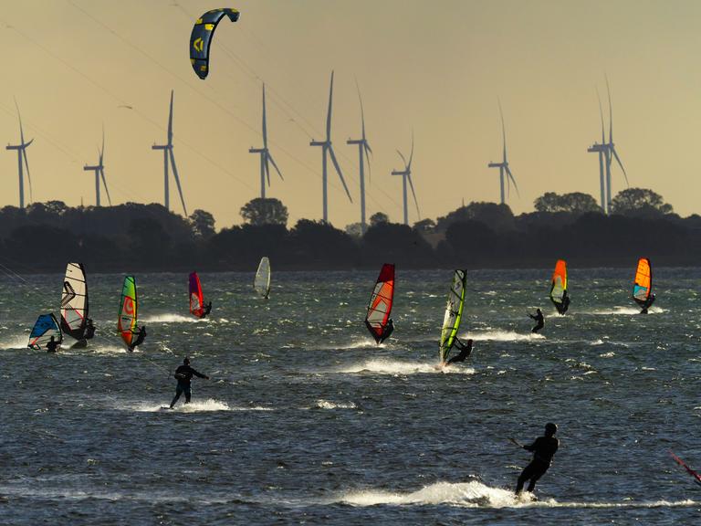 Surfer und und Kitesurfer an der Westküste von Fehmarn an der Ostsee. Im Hintergrund sind Windräder zu sehen. Vor dem kleinen Ort Gold auf Fehmarn liegt ein im weiten Umkreis beliebtes Surfrevier. Surfer und und Kitesurfer an der Westküste von Fehmarn an der Ostsee. Im Hintergrund sind Windräder zu sehen. Vor dem kleinen Ort Gold auf Fehmarn liegt ein im weiten Umkreis beliebtes Surfrevier.