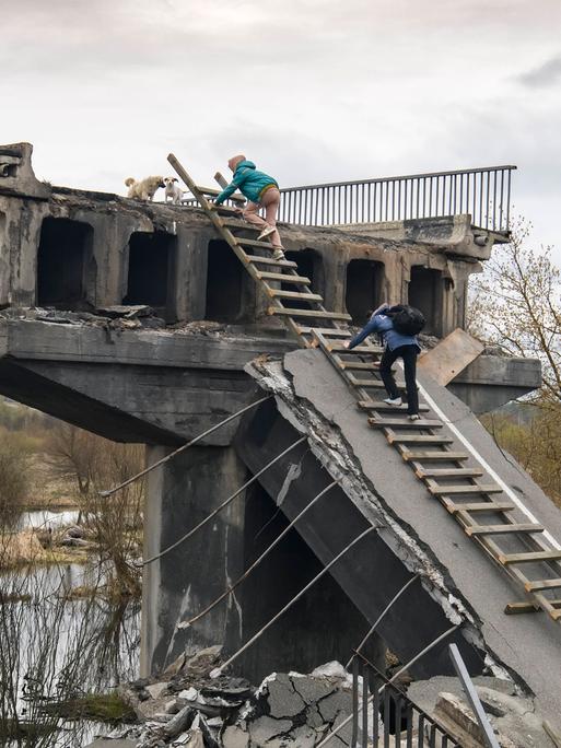 Zwei Ukrainer auf der Flucht klettern eine Leiter auf einer zerstörten Brücke hoch, Kukhari am 19.04.2022.